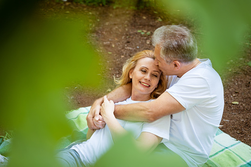 Mature adult happy couple in park hugging while sitting on plaid