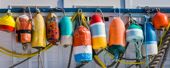 A collection of colorful old lobster buoys and  ropes hang on a wall in Provincetown, Massachusetts.