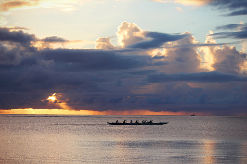 A small crew paddle a canoe across the open ocean at sunset