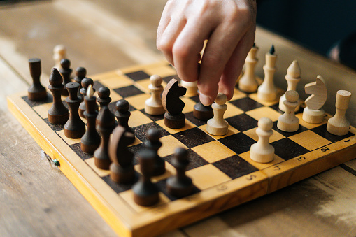 Close-up high-angle view of unrecognizable chess player performing move with pawn piece on wooden chessboard. Closeup of businessman making move with white pawn on chess board.