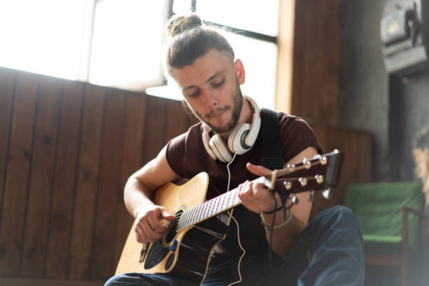 handsome young man playing acoustic guitar sitting floor living loft room - men artist guitarist guitar imagens e fotografias de stock