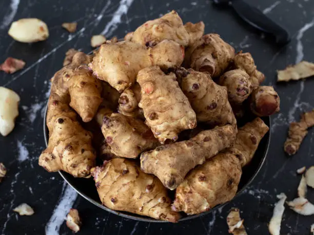 Fresh organic Jerusalem artichoke (root vegetable) in a bowl on a dark granite table. Top view, a closeup.