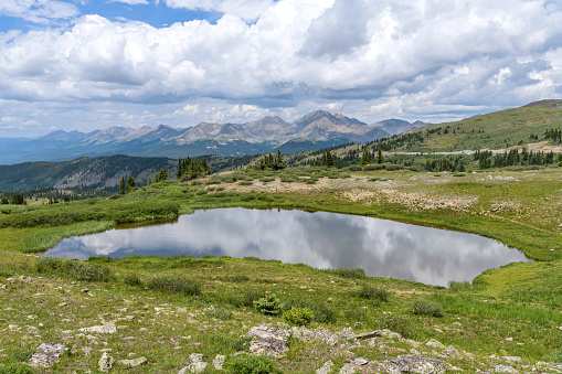 A panoramic view of a small pond at summit of Cottonwood Pass, surrounded by high peaks of Sawatch Range, on a calm Summer day. Buena Vista - Crested Butte, Colorado, USA.