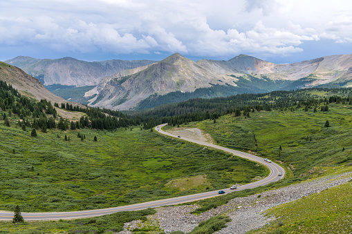 A panoramic Summer day view of a mountain road winding in a green valley at east of  the summit of Cottonwood Pass. Buena Vista - Crested Butte, Colorado, USA.