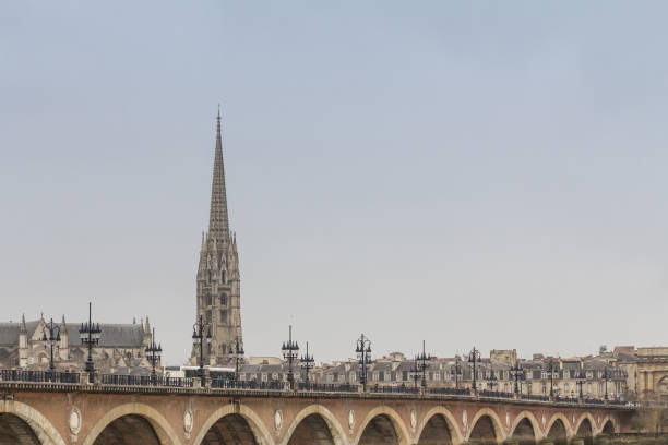 Panorama of the old town of Bordeaux, France, with the pont de pierre, or stone bridge, over the garonne river and the tower of the Basilique Saint Michel basilica a cloudy afternoon. "n"nPicture of a cloudy panorama of Bordeaux, France, with the stone bridge, or pont de pierre, in front of the basilique saint michel steeple. fleche stock pictures, royalty-free photos & images