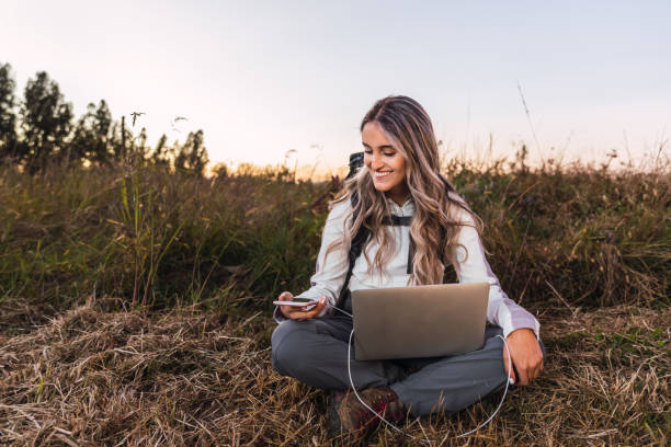Young woman with a backpack on, using a laptop to charge his smartphone. Teleworking. Digital nomad Young woman with a backpack on, using a laptop to charge his smartphone. Teleworking. Digital nomad digital nomad stock pictures, royalty-free photos & images