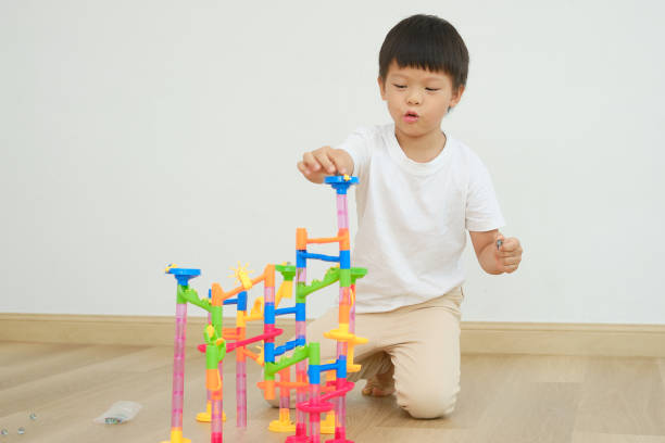 Asian boy child sitting on floor having fun playing with colorful plastic Marble Run Track Toy Set