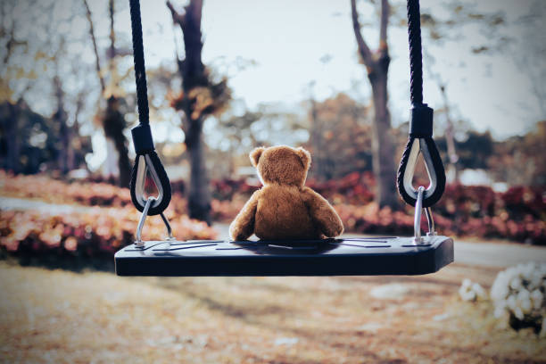 istock Teddy bear sitting on swing with flower park 1384699754
