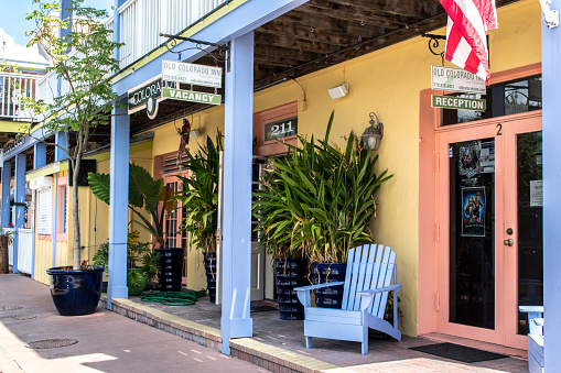 Historic Old Colorado Inn Hotel along the streets of historic downtown Stuart. Bright yellow building front, periwinkle blue painted trim, and an inviting porch chair by the front door.