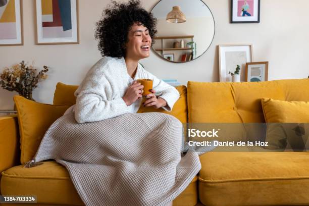 Happy African American Woman Enjoying Quiet Time At Home Laughing Drinking Morning Coffee Sitting On Sofa Copy Space Stock Photo - Download Image Now
