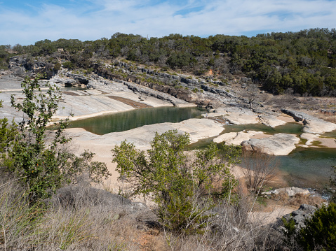 Overlook of Pedernales Falls with limestone formations in Pedernales Falls State Park in Texas. Two hikers stand by the upper pool.