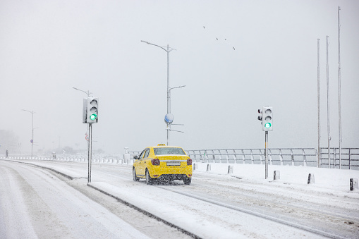 Yellow taxi drives on the road while it's snowing