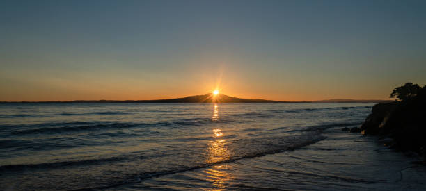 Sun rising at the top of Rangitoto Island, Milford Beach, Auckland. Sun rising at the top of Rangitoto Island, Milford Beach, Auckland. rangitoto island stock pictures, royalty-free photos & images