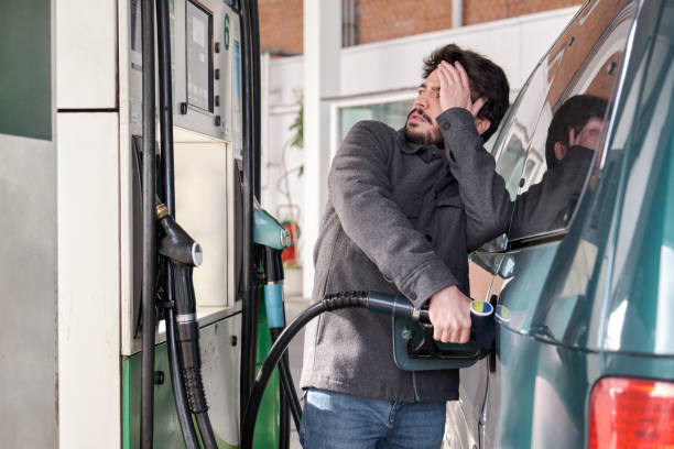 Young man refueling his vehicle while looking worried at the high gas prices. stock photo