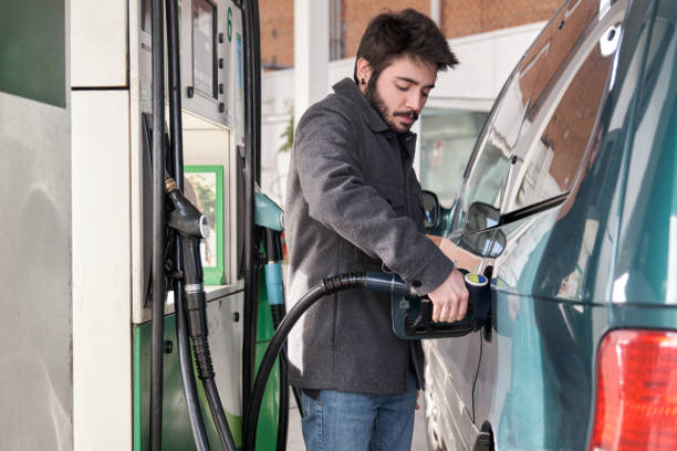 istock Young man putting nozzle into tank while refueling his car with gasoline. 1384741312