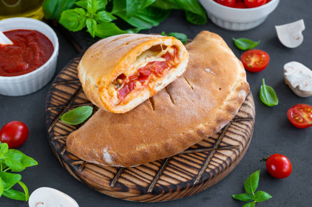 토마토 소스를 곁들인 전통적인 폐쇄형 이탈리아 칼존 피자, 모짜렐라 치즈, 버섯을 어두운 배경에 놓습니다. 선택적 초점 - pizza pastry crust stuffed cheese 뉴스 사진 이미지