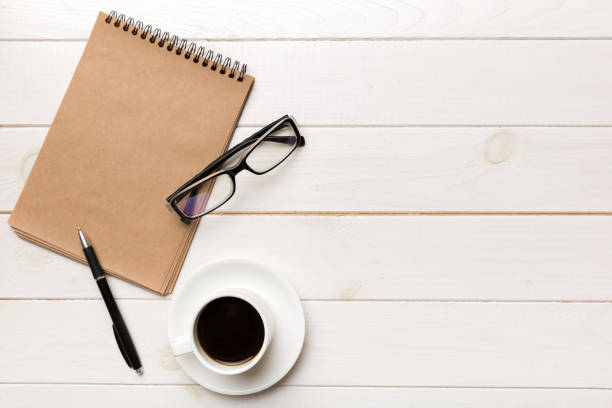 istock Modern office desk table with notebook and other supplies with cup of coffee. Blank notebook page for you design. Top view, flat lay 1384747926