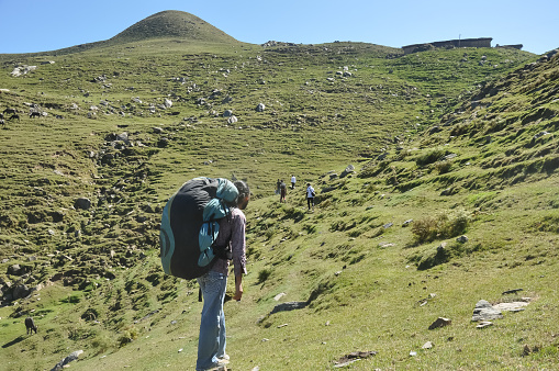 Back view of a male tourist walking on the mountain with his friends with carrying parachute backpack