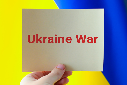 Ukraine War concept. Person holding paper with words 'Ukraine War' over ukrainian flag background. Russia Ukraine conflict conceptual. Stop War.