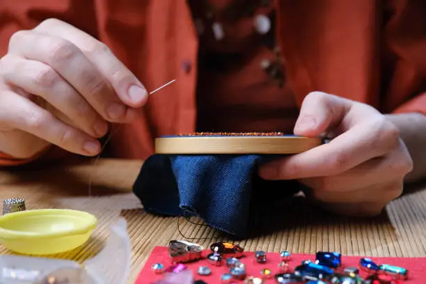 Photo of Hands of mature woman sitting at the desk and making bead and crystal jewelry at home