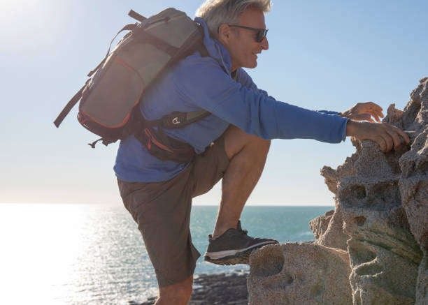 ハイカーは太平洋の上に崖をスクランブ�ル - climbing men sea cliff ストックフォトと画像