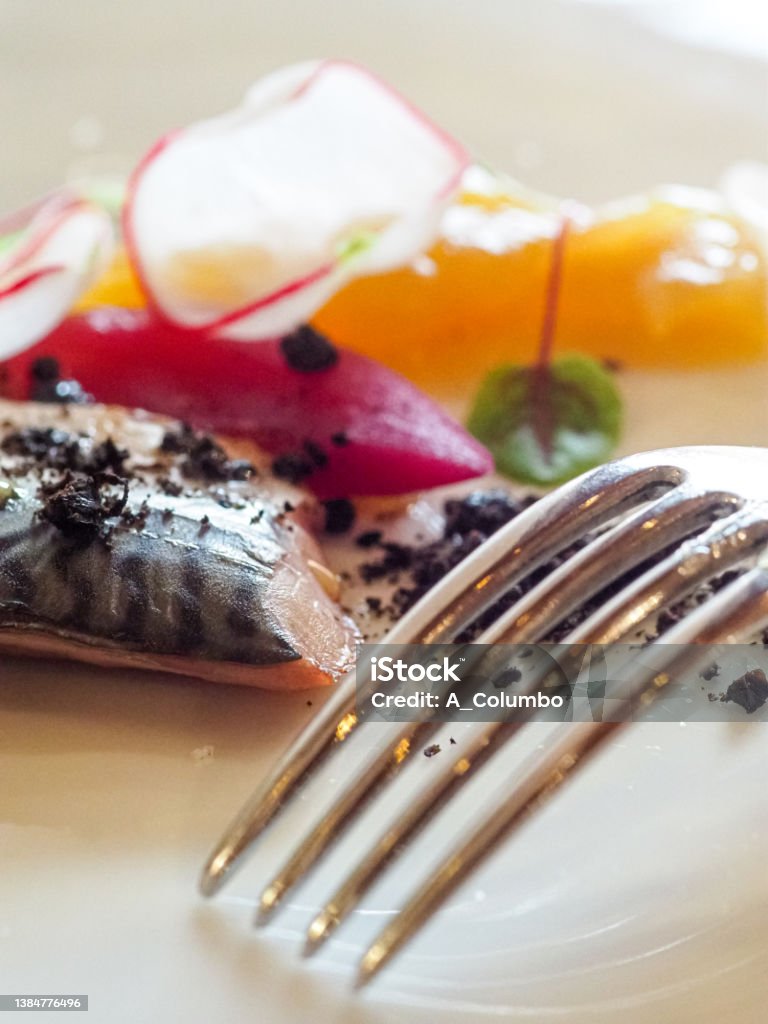mediterranean raw sea bass grilled fish filet, steamed potato, black olive sun dried powder, radish, caramelized red onions and lemon chutney on a porcelian fine italian design white dish with a glass of lugana white wine Color Image Stock Photo