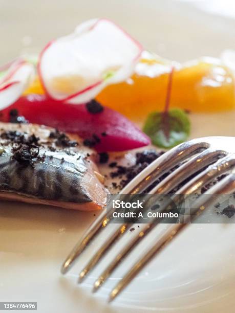 Mediterranean Raw Sea Bass Grilled Fish Filet Steamed Potato Black Olive Sun Dried Powder Radish Caramelized Red Onions And Lemon Chutney On A Porcelian Fine Italian Design White Dish With A Glass Of Lugana White Wine Stock Photo - Download Image Now