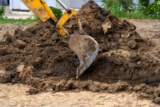 Photo of yellow bucket excavator levels pile of earth in front of country cottage