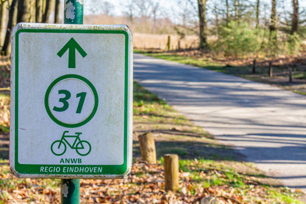 istock Bicycle route 31 sign, inscription: Region Eindhoven, a cycle path with bare trees in the blurred background, sunny day in the Dutch nature reserve Natuurpoort Vennenhorst, North Brabant, Netherlands 1384782193