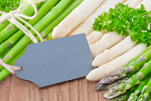 Seasonal fresh green and white asparagus with label on wooden background closeup