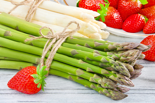 Fresh green and white asparagus with strawberries on wooden background closeup