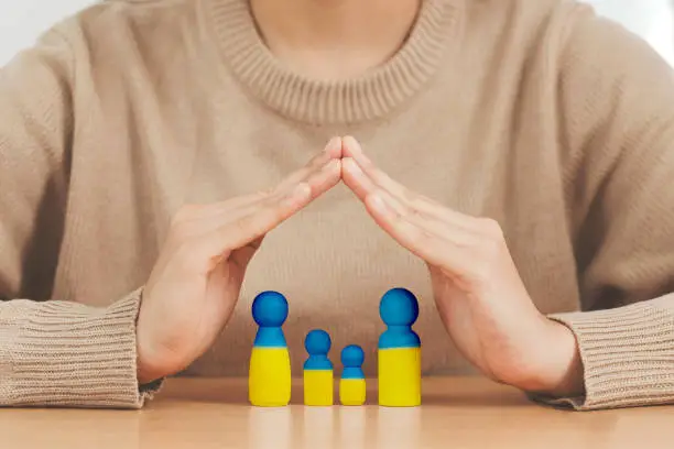 Love Ukraine concept. woman hands protecting Family  in the shape of a house with mother father and children painted in colors of Ukrainian flag in the home, provide housing to immigrants