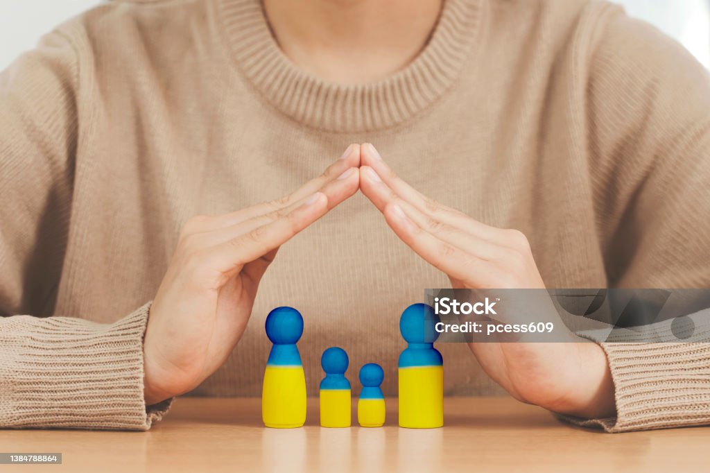 Love Ukraine concept. woman hands protecting Family  in the shape of a house with mother father and children painted in colors of Ukrainian flag in the home, provide housing to immigrants - 免版稅難民圖庫照片