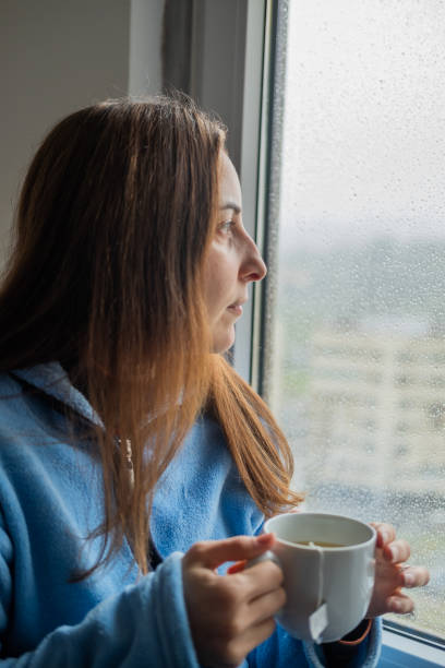 istock Woman drinking tea at the window while it rains outside 1384796890