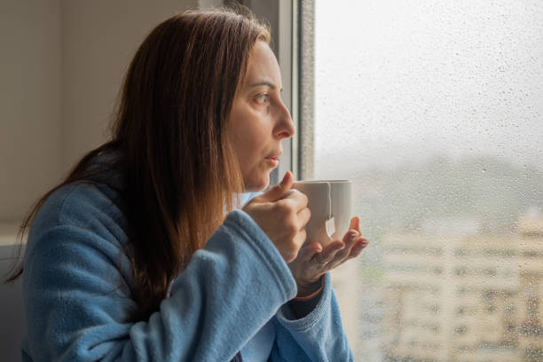 istock Woman drinking tea at the window while it rains outside 1384796946
