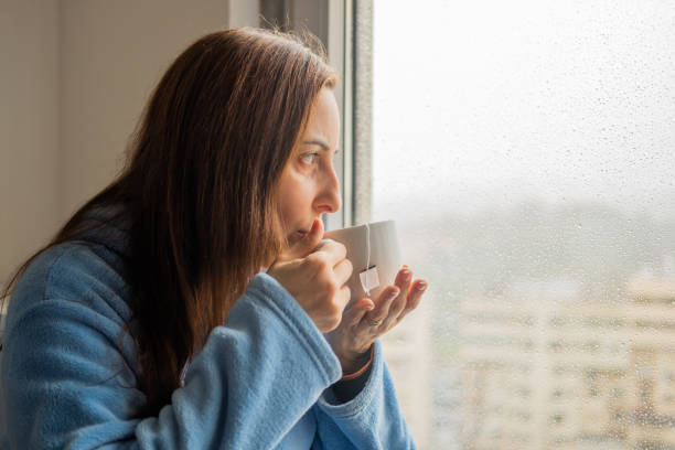 istock Woman drinking tea at the window while it rains outside 1384796961