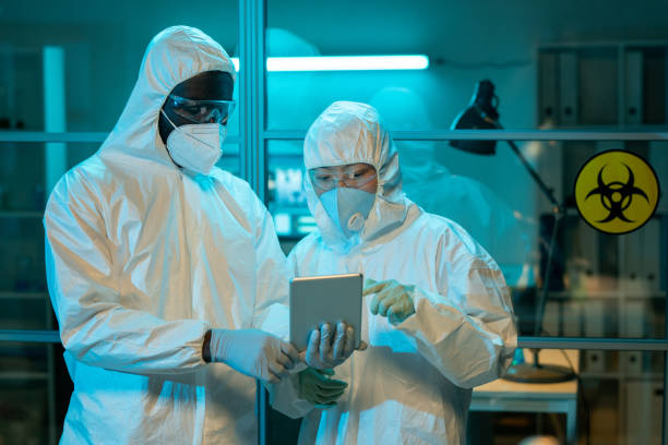 dwóch pracowników laboratorium naukowego omawiających dane kliniczne online - protective suit zdjęcia i obrazy z banku zdjęć