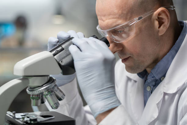 istock Gloved scientist or chemist researching chemical elements in microscope 1384798446