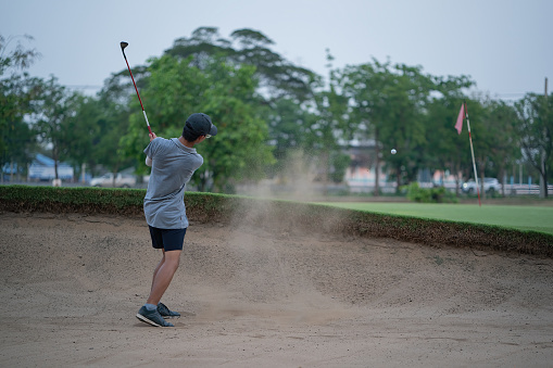 Boy golf player chipping from sand bunker onto green