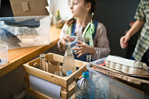 Mother teaching her children how to  separate plastic, glass and paper waste at home