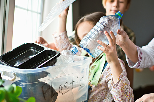 Mother teaching her children how to  separate plastic, glass and paper waste at home