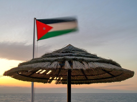 The sun sets over the Dead Sea and Palestine in the distance.  The umbrella is to provide shade for tourists.  This image was taken on a windy evening in March with a 1.6 second exposure.