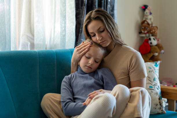 Woman and sad little daughter are sitting on couch and hugging stock photo