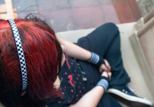 Punk emo girl, young adult with black red hair Punk emo girl, young adult with black red hair, sitting at a window frame, looking down, high angle view, horizontal black hair emo girl stock pictures, royalty-free photos & images