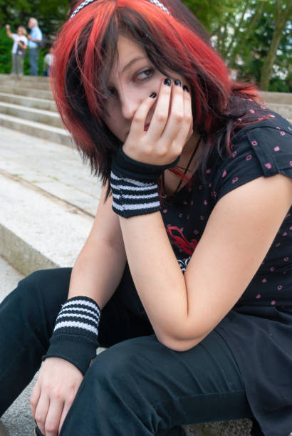 Punk emo girl, young adult with black red hair Punk emo girl, young adult with black red hair, sitting on a staircase outdoors, holding her head, looking away, horizontal black hair emo girl stock pictures, royalty-free photos & images
