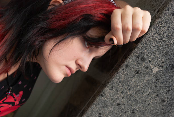 Punk emo girl, young adult with black red hair Punk emo girl, young adult with black red hair, holindg her head against a concrete wall, close-up, horizontal black hair emo girl stock pictures, royalty-free photos & images
