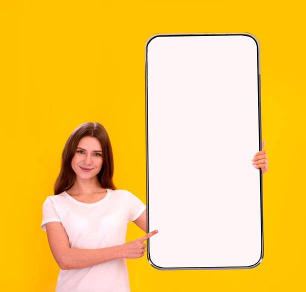 istock Young Beautiful Woman Holding And Pointing At Cellphone With Blank Screen 1384825344