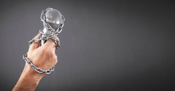 istock Human hand holding microphone tied with chains. 1384828239
