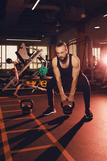 istock Fit young man with a beard in sportswear focused on lifting kettlebells while exercising in the gym 1384831469