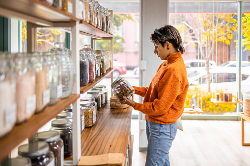 A young Latin woman standing and holding jar in a zero waste store.